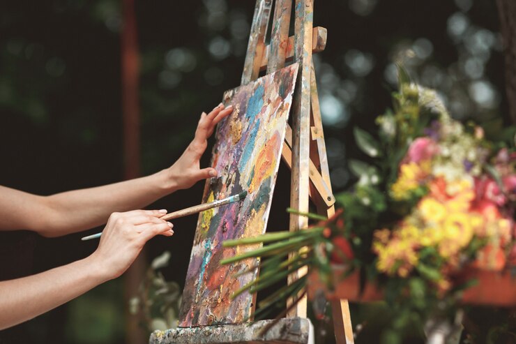 female hands with a brush painting a picture on an easel, with a bouquet of flowers in the foreground