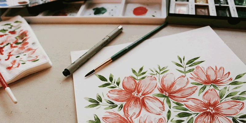 a flower drawing with a brush, pencil, paints, palette, and a napkin covered with paint