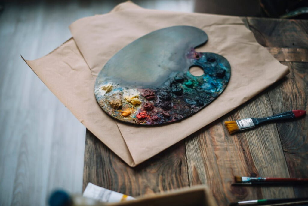 color palette with paints and brushes near it on a dark wooden table